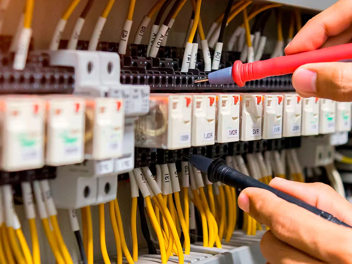 Técnico realizando mantenimiento con multímetro sobre bornas identificadas de un cuadro eléctrico